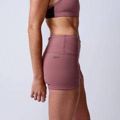 Side view of a woman wearing mauve high-waisted workout shorts with GORUCK logo and matching sports bra