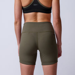 A woman in a sports bra and olive green Women’s Biker Shorts - ToughFlex stands with her back to the camera, highlighting her athletic style.