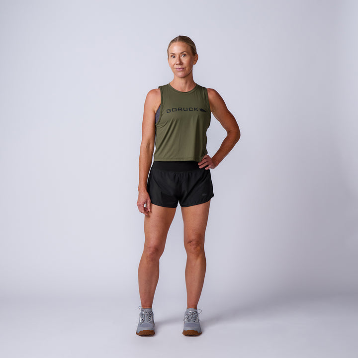 A woman poses in the Women’s Performance Tank - ToughMesh in olive and black shorts, standing against a plain light background.