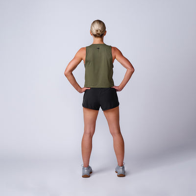 Woman standing with hands on hips, facing away, wearing the Women’s Performance Tank - ToughMesh in athletic wear, on a plain background.
