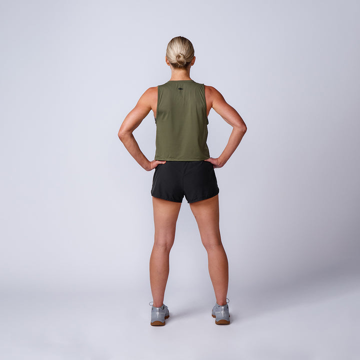 Woman standing with hands on hips, facing away, wearing the Women’s Performance Tank - ToughMesh in athletic wear, on a plain background.