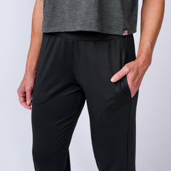 A person is shown from the shoulders down wearing a gray shirt and the Women’s Training Performance Joggers in black, with one hand in their pocket.