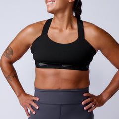 Woman smiling with hands on hips, wearing the Power Bra - Toughflex for high-impact support and gray leggings made from ToughStretch Fabric, against a plain background.