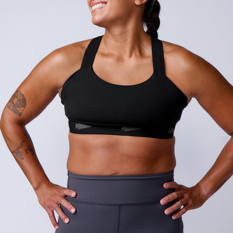 Woman smiling with hands on hips, wearing the Power Bra - Toughflex for high-impact support and gray leggings made from ToughStretch Fabric, against a plain background.