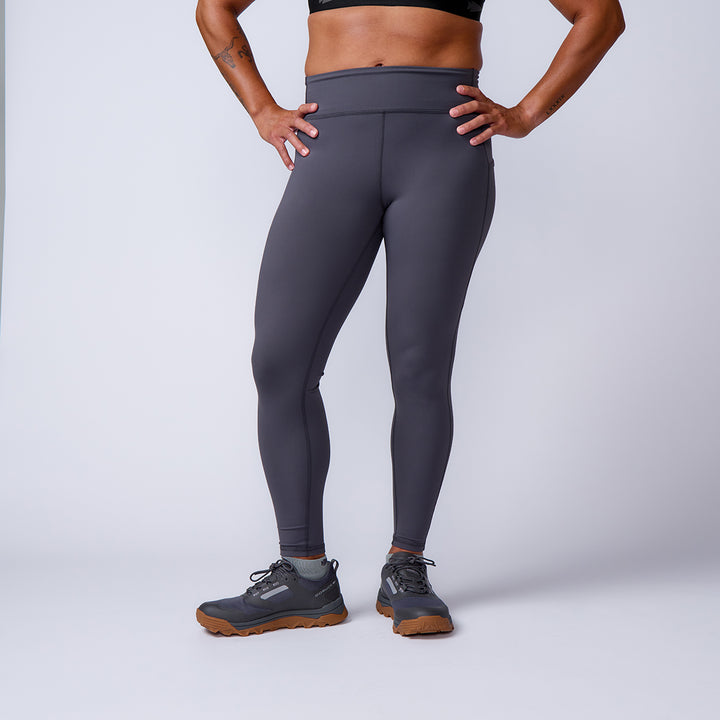 A person wearing Women’s Training Leggings Pocket - ToughFlex and gray sneakers poses with hands on hips against a plain background.
