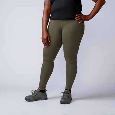 A woman wearing the Women’s Training Leggings Pocket - ToughFlex in olive green, paired with a black top and green shoes, stands with one hand on her hip against a plain background.
