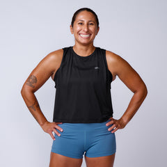 Smiling woman in athletic wear stands with hands on hips against a plain background, showcasing the Women’s USA Performance Tank made with featherweight ToughMesh fabric.