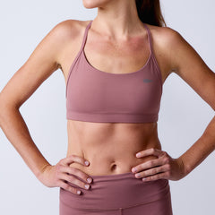 A woman models the Stealth Bra - ToughFlex in mauve, a minimalist sports bra and leggings set offering lightweight support, with one hand on her hip against a plain background.