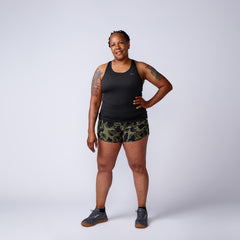 A smiling woman in athletic wear models Women’s Training Shorts - ToughStretch, featuring camo design and squat-proof durability, posing confidently against a plain light background.