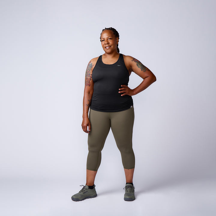 Person in athletic wear stands confidently with one hand on hip, smiling against a plain background, showcasing Women’s Training Leggings Pocket - ToughFlex—durable leggings designed for any workout.