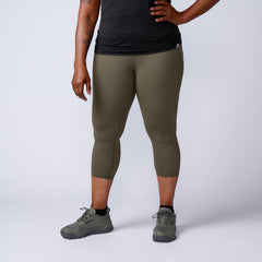Person wearing olive green athletic capri leggings, black top, and green GORUCK shoes on white background