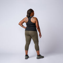 Rear view of woman with tattoos wearing black tank top, olive green leggings, and gray shoes in studio