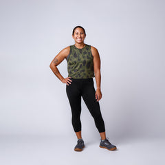 Smiling woman in camo tank top, black leggings, and gray athletic shoes posing against white backdrop