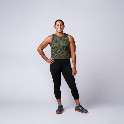 A woman in athletic wear smiles with one hand on her hip against a plain light background, modeling the Women’s Training Leggings Pocket - ToughFlex, perfect for any workout.