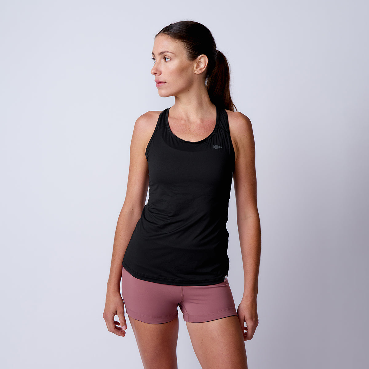 A woman wearing the Women’s Racerback Tank - ToughMesh and mauve shorts stands facing left against a plain light background.