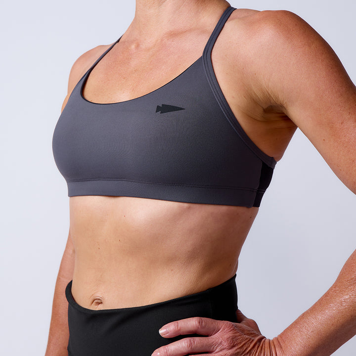 Woman wearing the Stealth Bra - ToughFlex in gray with black leggings, standing with one hand on her hip against a plain background.