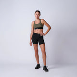 Woman wearing GORUCK olive sports bra and black shorts in studio for rucking gear showcase