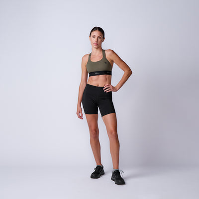 Woman in Women’s Biker Shorts - ToughFlex stands confidently against a plain light background, paired with a sports bra and sneakers.