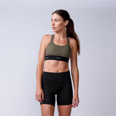 A woman stands confidently against a plain light gray background, wearing Women’s Biker Shorts - ToughFlex and a green sports bra.