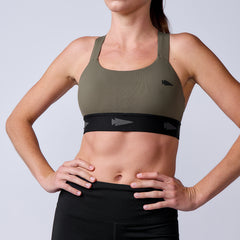Woman wearing the Power Bra - Toughflex in olive green with black accents and matching black leggings, hands on hips. Designed with ToughStretch Fabric for high-impact support.