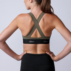 Woman wearing the Power Bra - Toughflex with a crisscross back and black leggings, made from durable ToughStretch fabric, facing away with hands on hips.