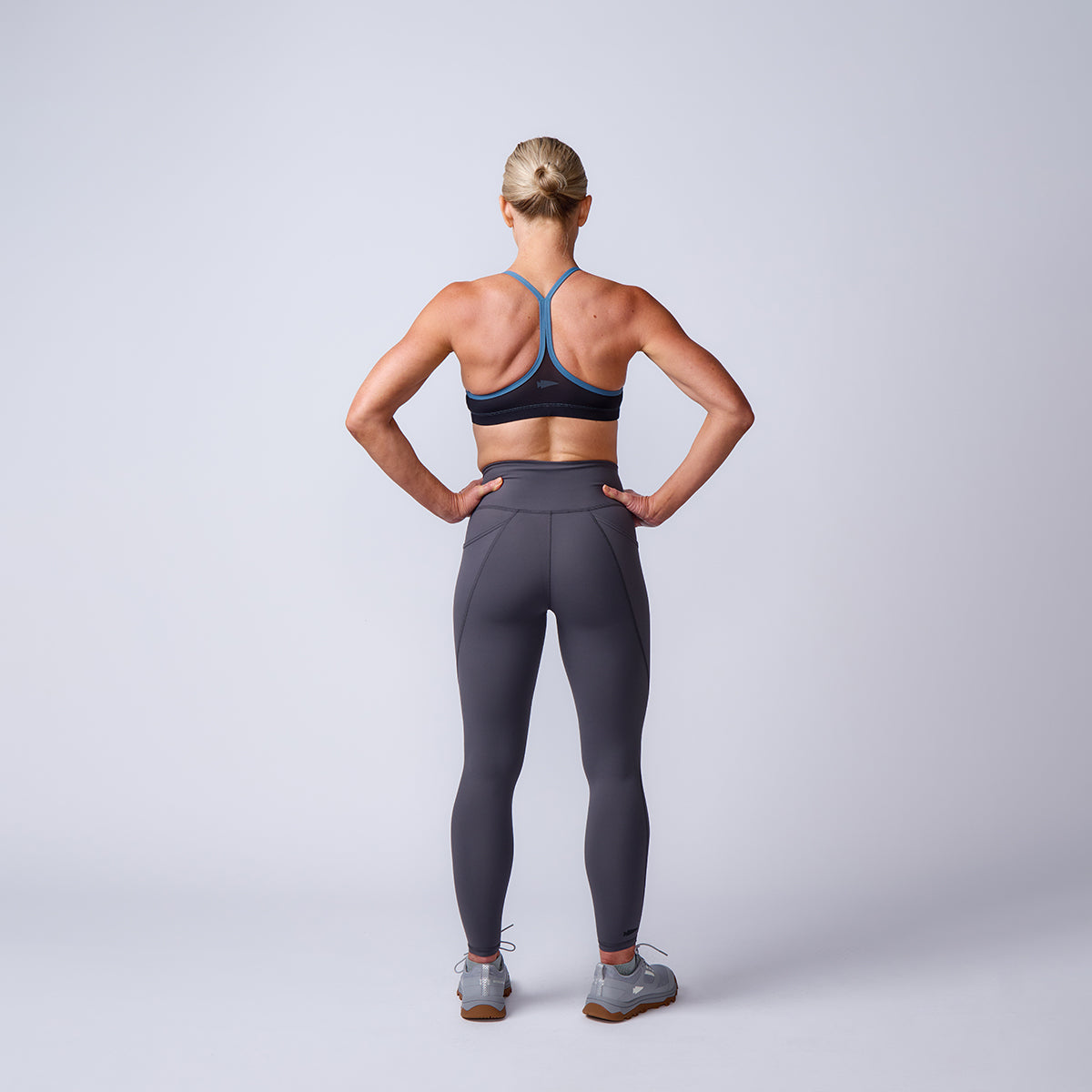 Woman in athletic wear stands with hands on hips, showcasing Women’s Training Leggings Pocket - ToughFlex against a plain light background.