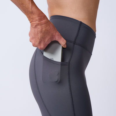 A person slips a smartphone into the side pocket of dark gray Women’s Training Leggings Pocket - ToughFlex, highlighting these durable workout leggings designed for convenience.