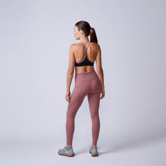 Woman wears mauve Women’s Training Leggings Pocket - ToughFlex and a black sports bra, standing facing away in a studio with a plain background.