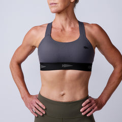 Woman in a gray Power Bra - Toughflex and olive leggings, both made from durable ToughStretch Fabric, stands with hands on hips against a plain background.