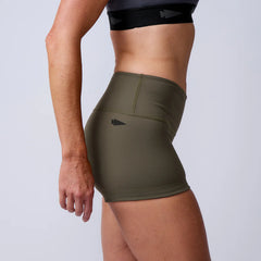 Side view of a person wearing olive green high-waisted athletic shorts with a black logo, and a black sports bra, studio background