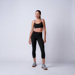 Fit woman in black sports bra and leggings with gray sneakers in a minimalist studio background