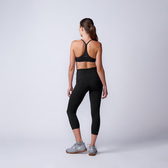 Woman in black sports bra and leggings with gray GORUCK sneakers standing against white background