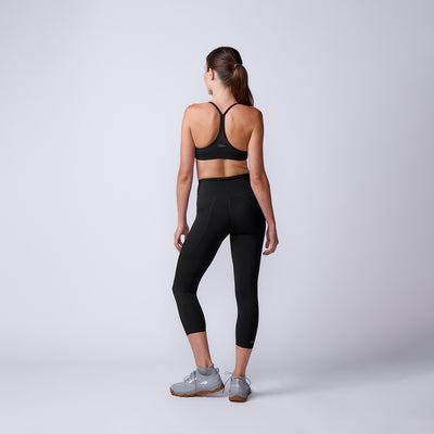 Woman wearing Women’s Training Leggings Pocket - ToughFlex in black with a sports bra, standing on a plain background, facing away with her hair in a ponytail.