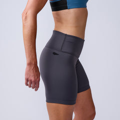 Woman in athletic wear, side view, wearing gray Women’s Biker Shorts - ToughFlex and a blue sports bra.