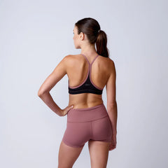 Rear view of woman in black and mauve sports bra and mauve athletic shorts on plain background