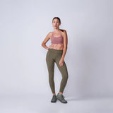 Woman wearing GORUCK olive green leggings, pink sports bra, and trail shoes in studio.