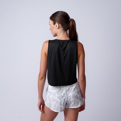 Woman with brown hair in a ponytail wears a black tank top and ToughStretch Women’s Training Shorts with a white pattern, facing away.