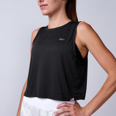A woman stands with one hand on her hip against a plain background, wearing the Women’s USA Performance Tank in black, crafted from featherweight ToughMesh fabric, paired with white shorts.