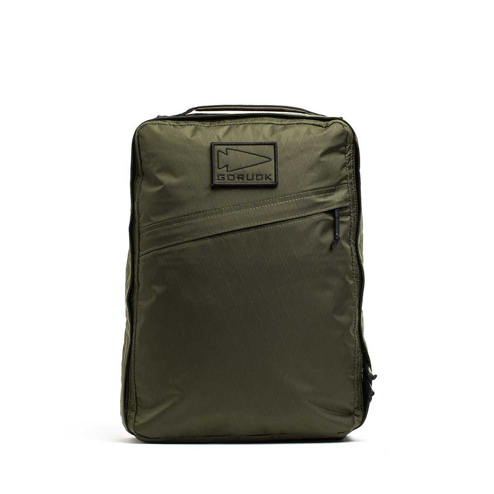 The GR0 - X-PAC is an olive green backpack made from lightweight, waterproof rucksack material, featuring a diagonal zip pocket and a rectangular "GORUCK" patch on the front.