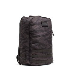 The GR1 USA - Cordura is a black and gray camouflage everyday carry rucksack, featuring a front zipper pocket and Special Forces grade webbing on the lower half, inspired by GORUCK Challenge designs.