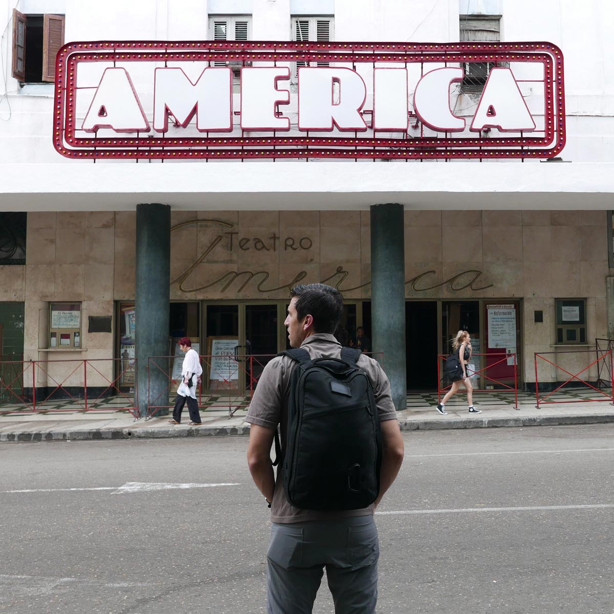 A man with a backpack stands in front of the Teatro América building.