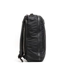 Side view of a black durable GORUCK backpack with multiple zippered compartments on white background