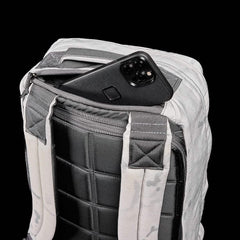 The GR1 backpack, with a phone partially tucked into its zippered pocket, is shown against a black background, highlighting its rugged Special Forces–inspired design.