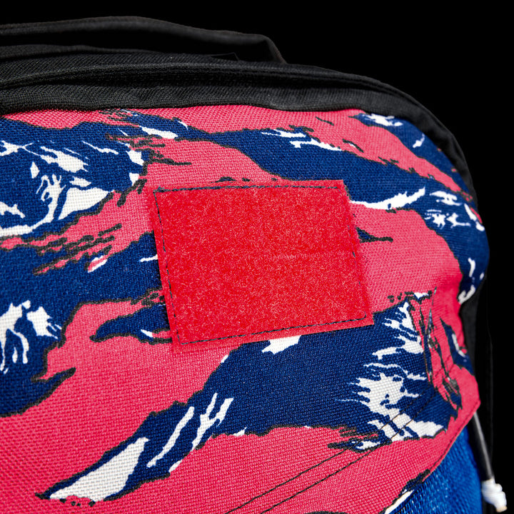 Close-up of the GR1 Shooter 26L - Built by SCARS, made from durable CORDURA® fabric, featuring a red Velcro patch and a blue, pink, and white abstract pattern—crafted for adventurous SCARS team members.
