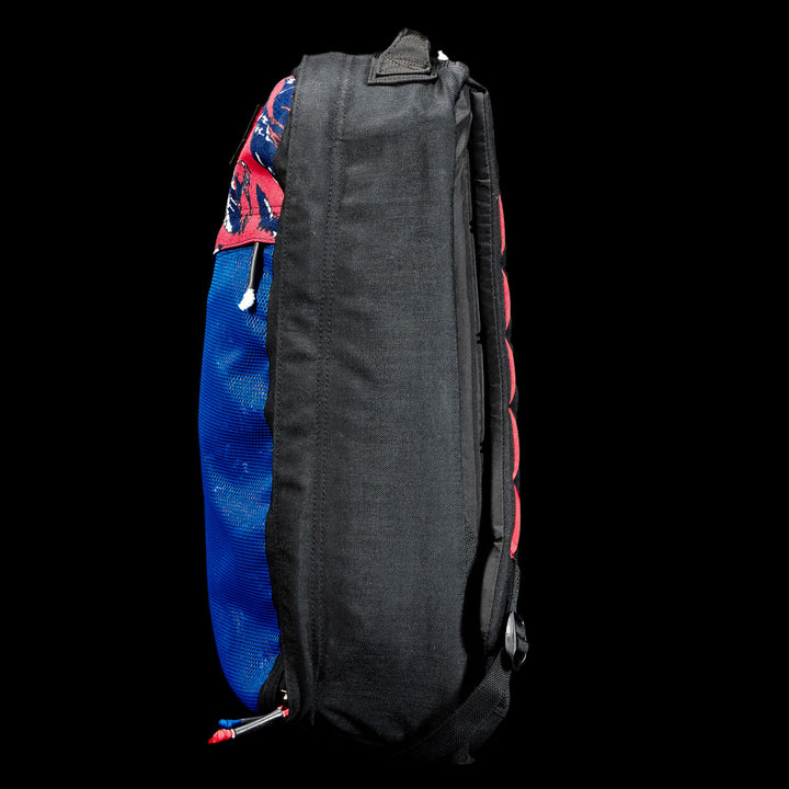 Side view of a blue and black GR1 Shooter 26L - Built by Scars backpack with red accents, graphic top design, and durable CORDURA® fabric construction.