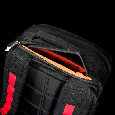 The GR1 Shooter 26L - Built by Scars backpack features a durable CORDURA® exterior, red straps, an open compartment with orange lining, and fits a black smartphone inside.