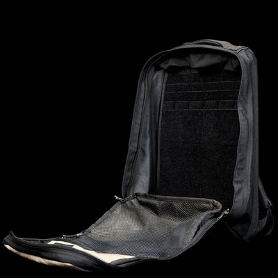 A black GR1 Shooter 26L - Built by Scars backpack, crafted from rugged CORDURA® fabric, sits open against a black background, revealing its empty main compartment and mesh pocket.