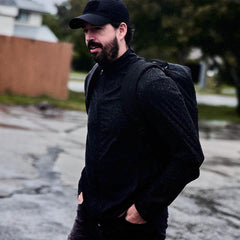 Man wearing black cap and jacket with GORUCK backpack walking outdoors on a rainy day