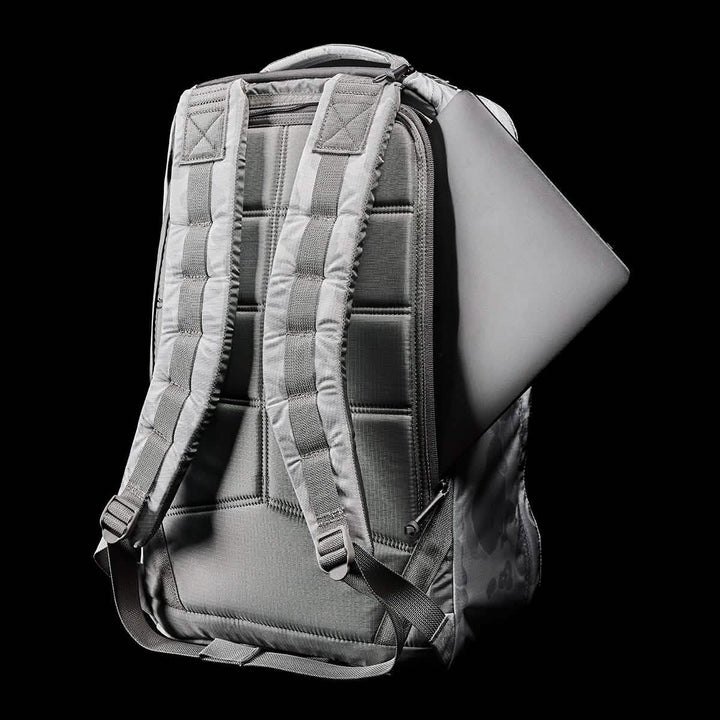 The GR1 USA - Ripstop ROBIC® from GORUCK is displayed from the back, showcasing its sleek, ultra-lightweight design with padded straps. A laptop is visible emerging from one of its water-resistant compartments against a black background.