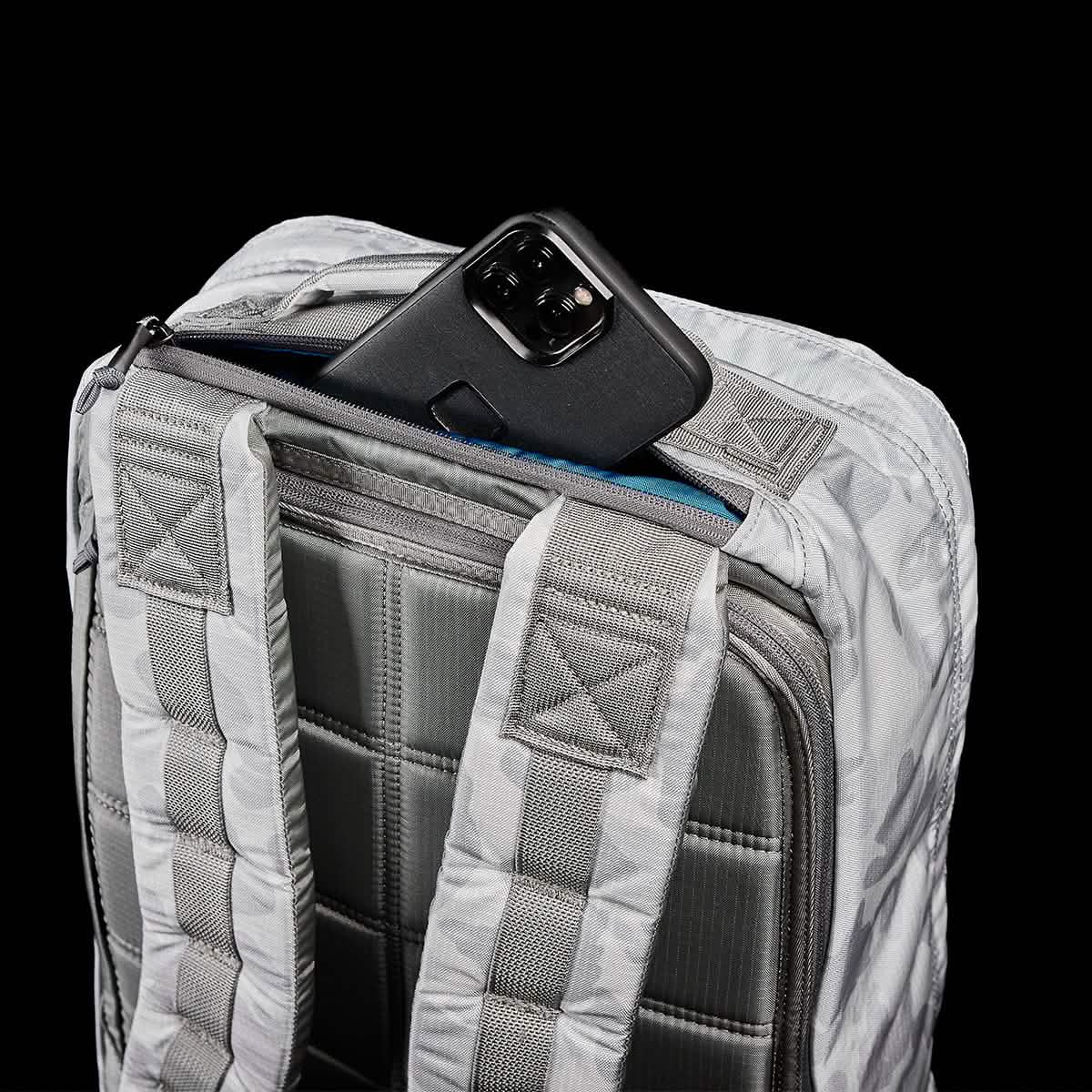 A GR1 USA - Ripstop ROBIC® rucksack by GORUCK in gray, showcasing its ultra-lightweight design with padded straps and a quilted back panel, is partially open to reveal a black smartphone nestled inside a pocket. The solid black background brings out the details of the rucksack.